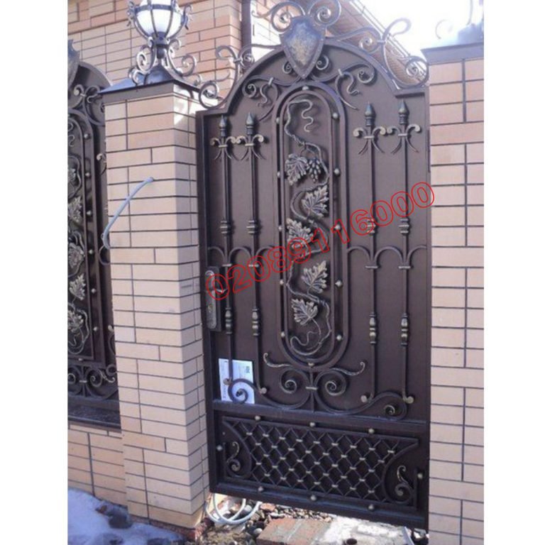 Ornate wrought iron garden gate with arched top and grapevine scrollwork detail set in brick pillars