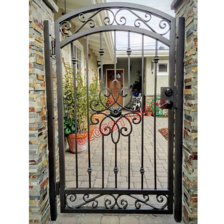 Wrought iron garden gate with arched top and scroll detail fitted between stone pillars