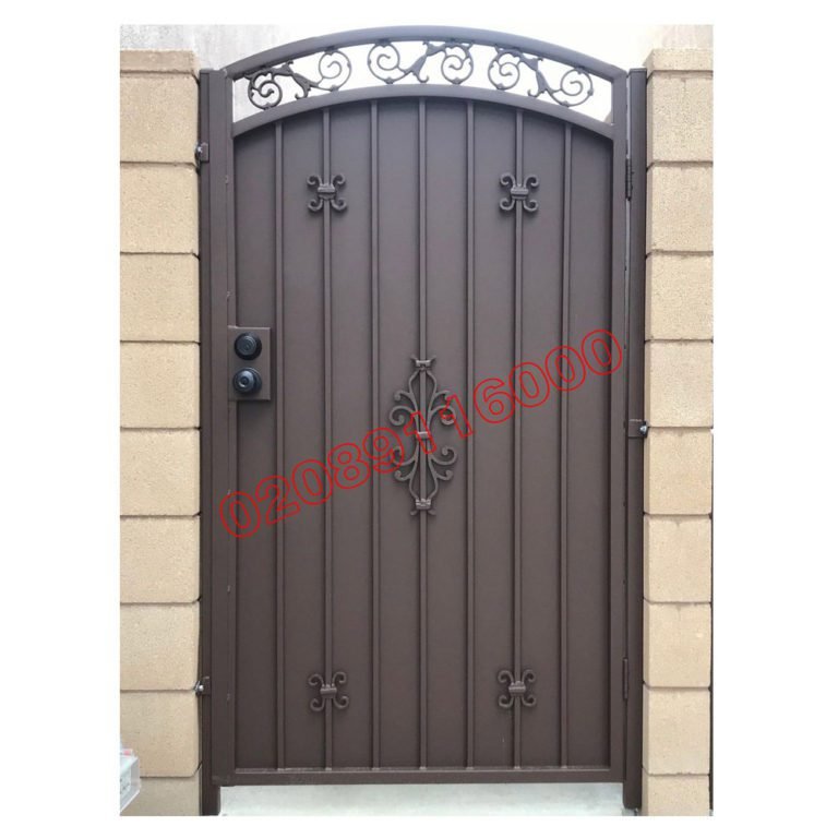 Brown metal garden gate with privacy panel, arched scrollwork top and decorative fleur-de-lis details