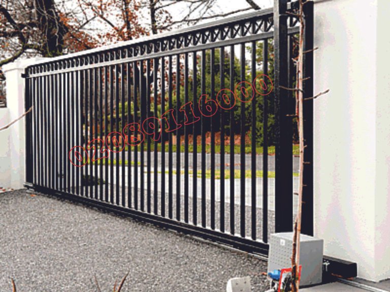 Black metal cantilever sliding gate with cross-lattice top rail on gravel driveway