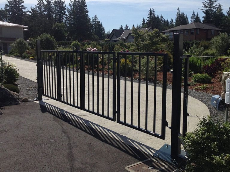Black metal bifold driveway gate with vertical bars folded open on concrete driveway