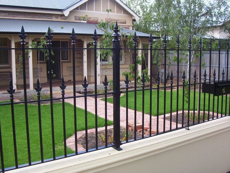 Black spear top metal railings with fleur-de-lis finials on a low garden wall