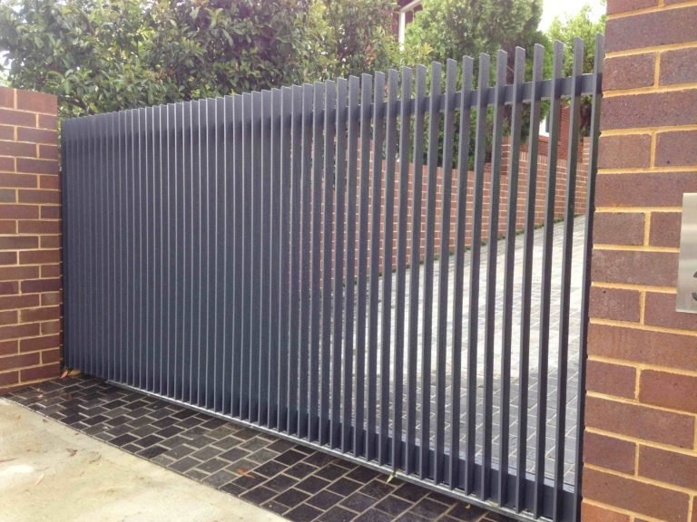 Dark grey metal sliding driveway gate with vertical slats between brick piers