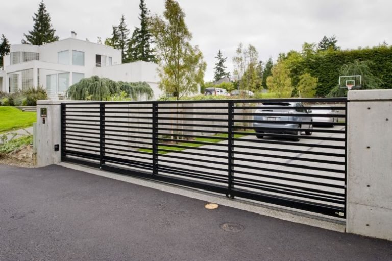 Black horizontal slat metal sliding driveway gate between concrete pillars at a modern house