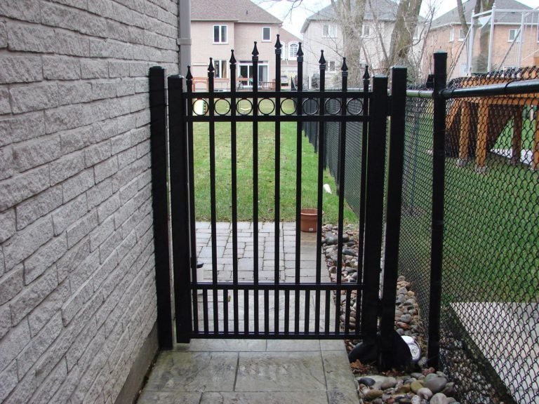 Black metal side gate with spear finials and ring detail fitted beside a stone wall