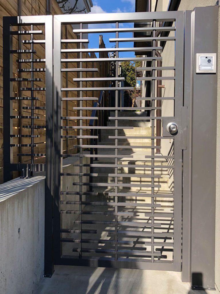Dark grey metal side gate with horizontal slat design and cylinder lock fitted to side passage