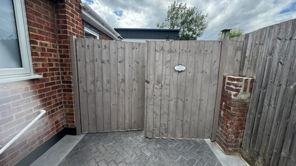 Weathered grey timber side gate and fence panel between brick house and garden wall