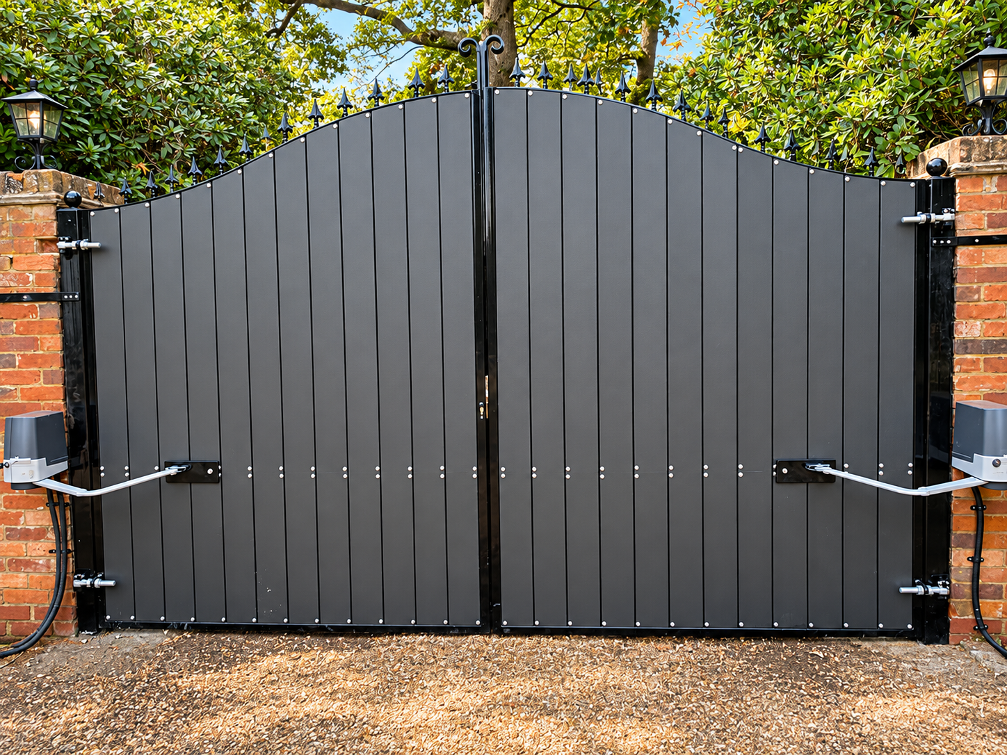 Dark grey arched driveway gates with black frames, spear finials and visible opener arms.