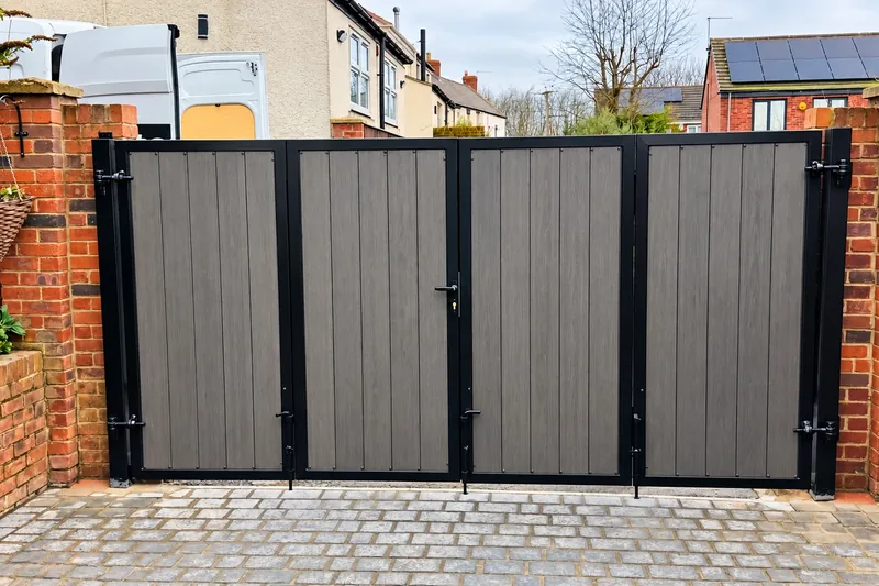 Grey composite driveway gate with a black frame between brick pillars