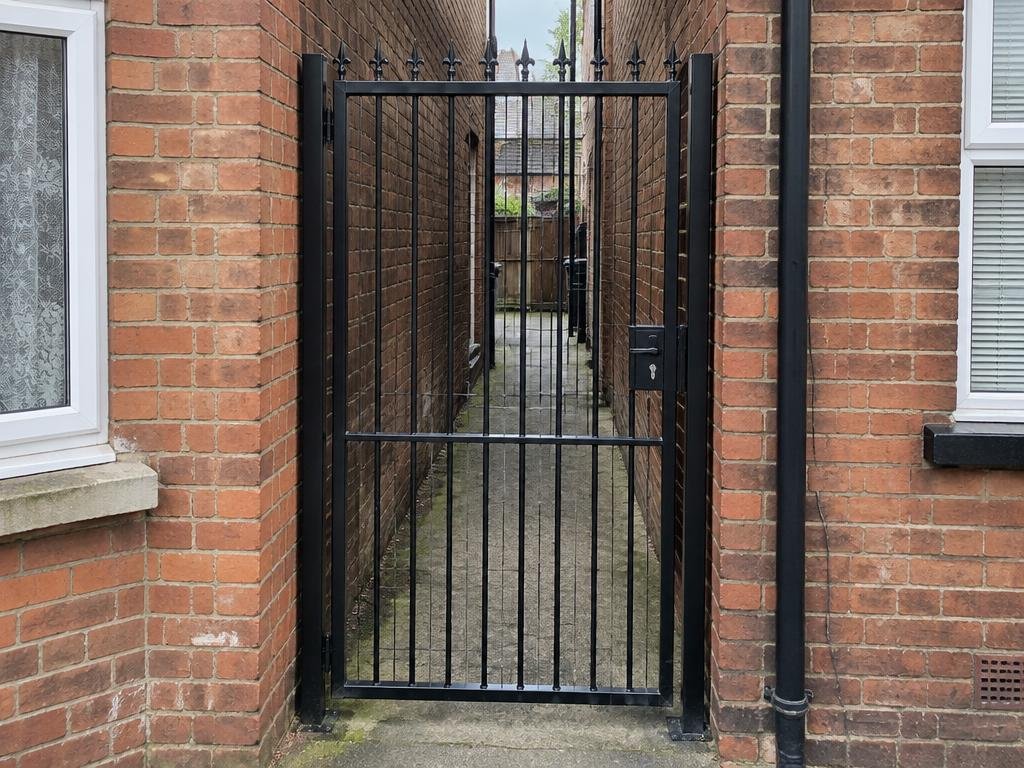 Tall black metal gate closing a brick passage between houses